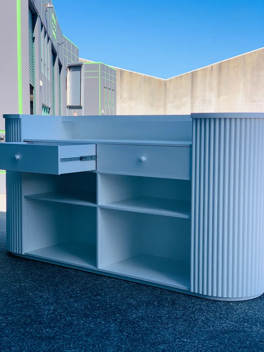 Rear of a blue-grey reception desk showing open shelving under the counter
