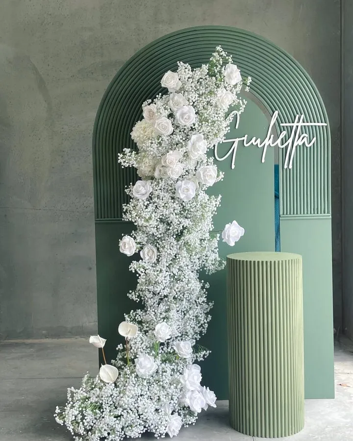 Deep green arch with a cascade of white roses and baby's breath, and a matching fluted plinth