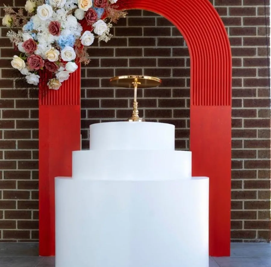 Red arch backdrop against a dark brick wall with white stepped plinths in front
