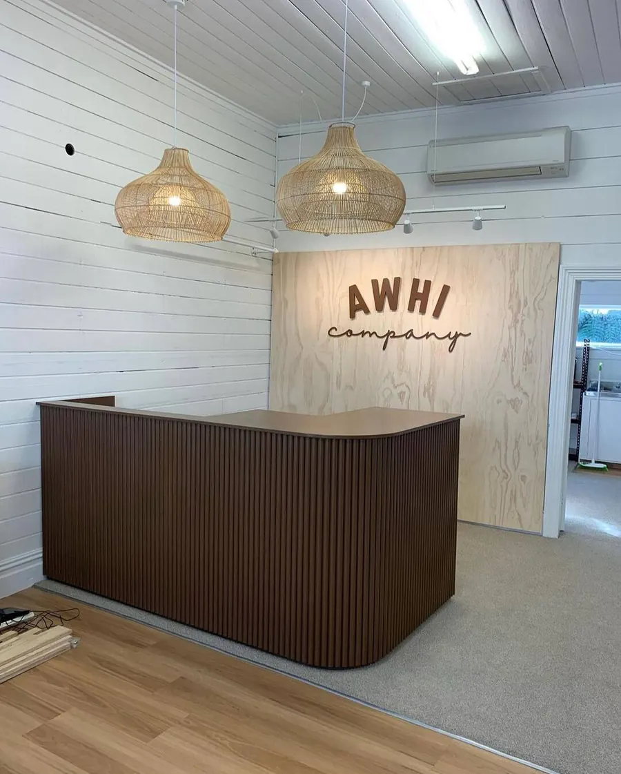 Dark timber-look reception desk under rattan pendants in a white lined office