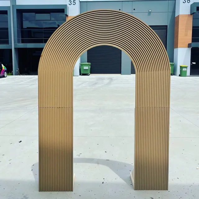 Tall fluted arch finished in gold, standing on a concrete floor