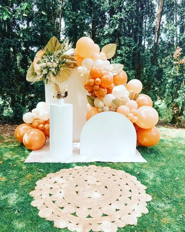 Outdoor arch set on a lawn with an orange and white balloon garland