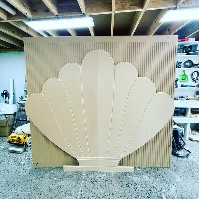 Large scalloped shell backdrop panel in raw board, standing in the workshop