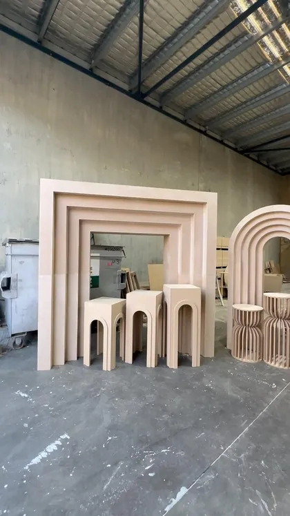 A row of arch frames, plinths and a fluted cylinder in raw board, standing in the warehouse