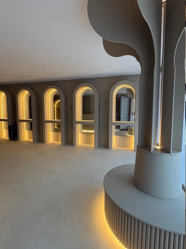 A corridor of backlit arched niches with a fluted column at its centre