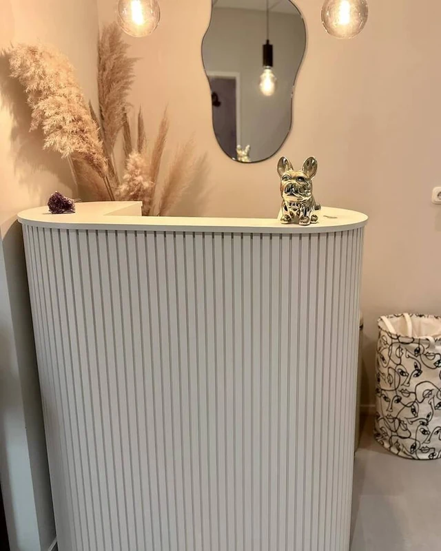 Grey fluted reception counter styled with dried flowers beneath a wavy mirror