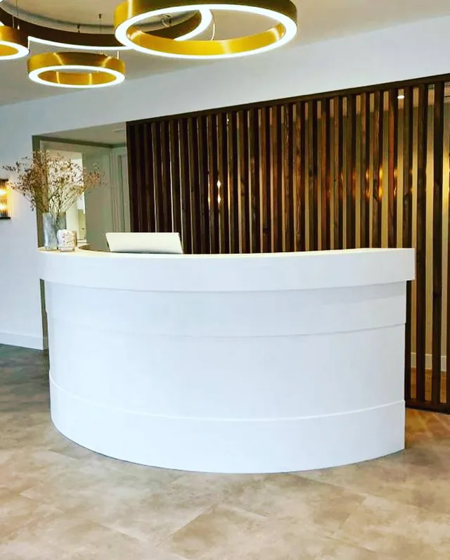 White curved reception counter under gold ring pendants with a slatted wall behind