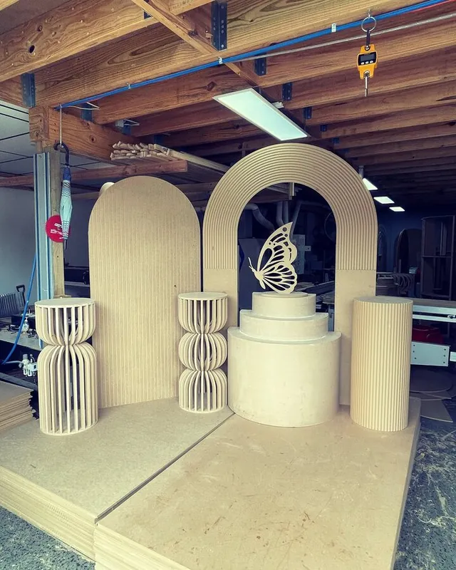 Arch backdrop, plinths and a cut butterfly in raw board, set up on the workshop floor