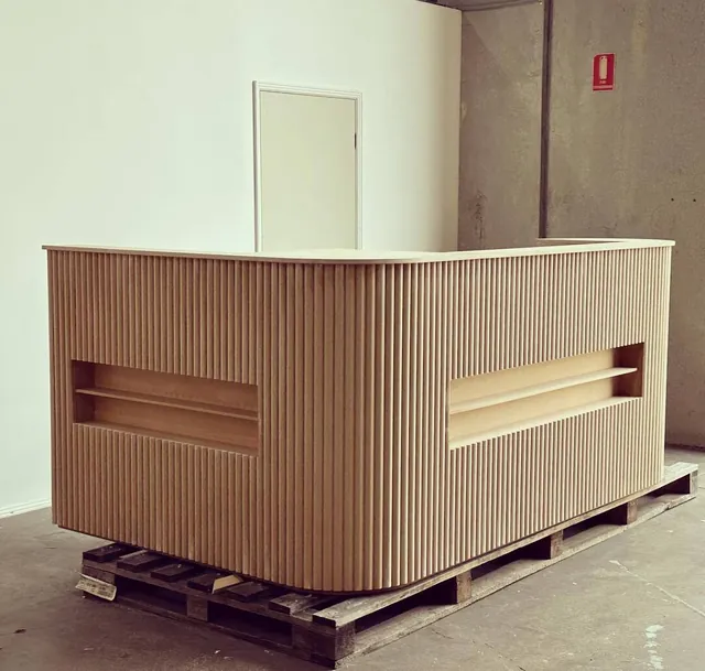 Timber-look fluted reception desk on a pallet with a recessed light bar in the front